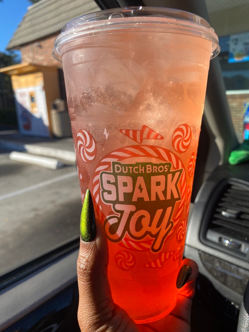 a hand with a green nail holding a lemonade cup that says Dutch Bros spark joy.